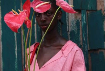 Retrato de modelo negra usando roupa rosa e segurando hastes de antúrios