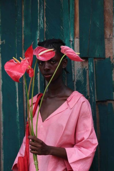 Retrato de modelo negra usando roupa rosa e segurando hastes de antúrios