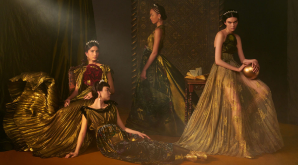 Quatro modelos com vestidos longos em tons de dourado, da Dior, contra um fundo escuro