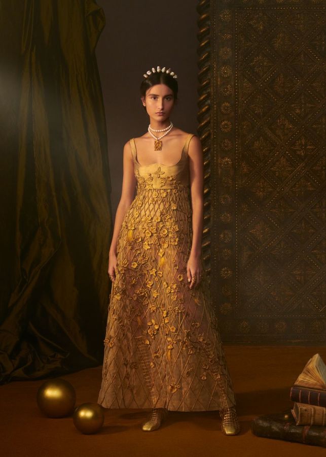 Modelo usando um vestido longo, dourado, em pé contra um fundo escuro